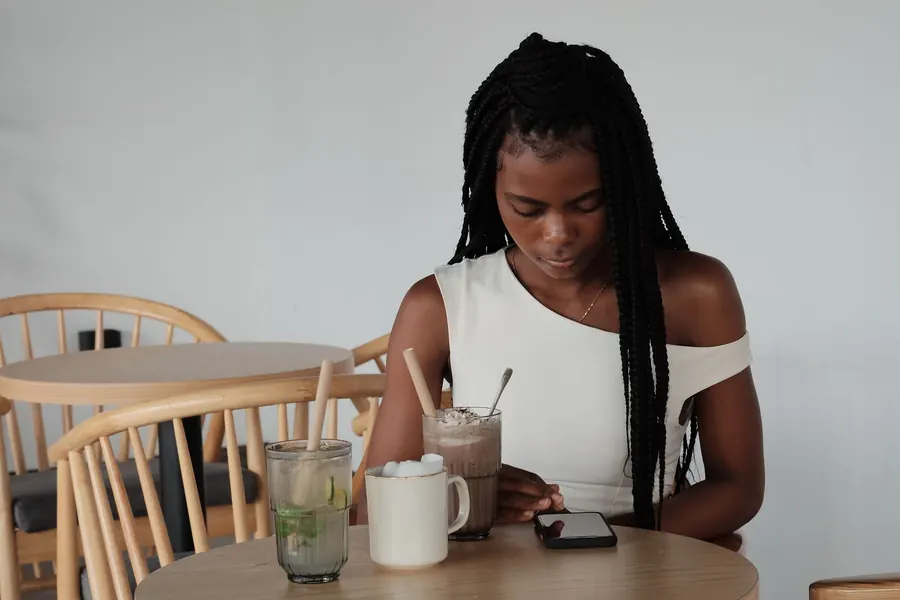 Gast sitzt am Tisch in einem hellen Café und schaut auf sein Smartphone
